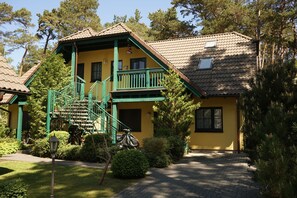 A yellow building with a green balcony, a staircase, and a covered porch.
