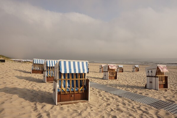 Beach chairs with striped awnings, a sandy beach, and a clear sky.