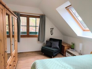 A room with a loft bed, a desk, a chair, a window with curtains, and a skylight.