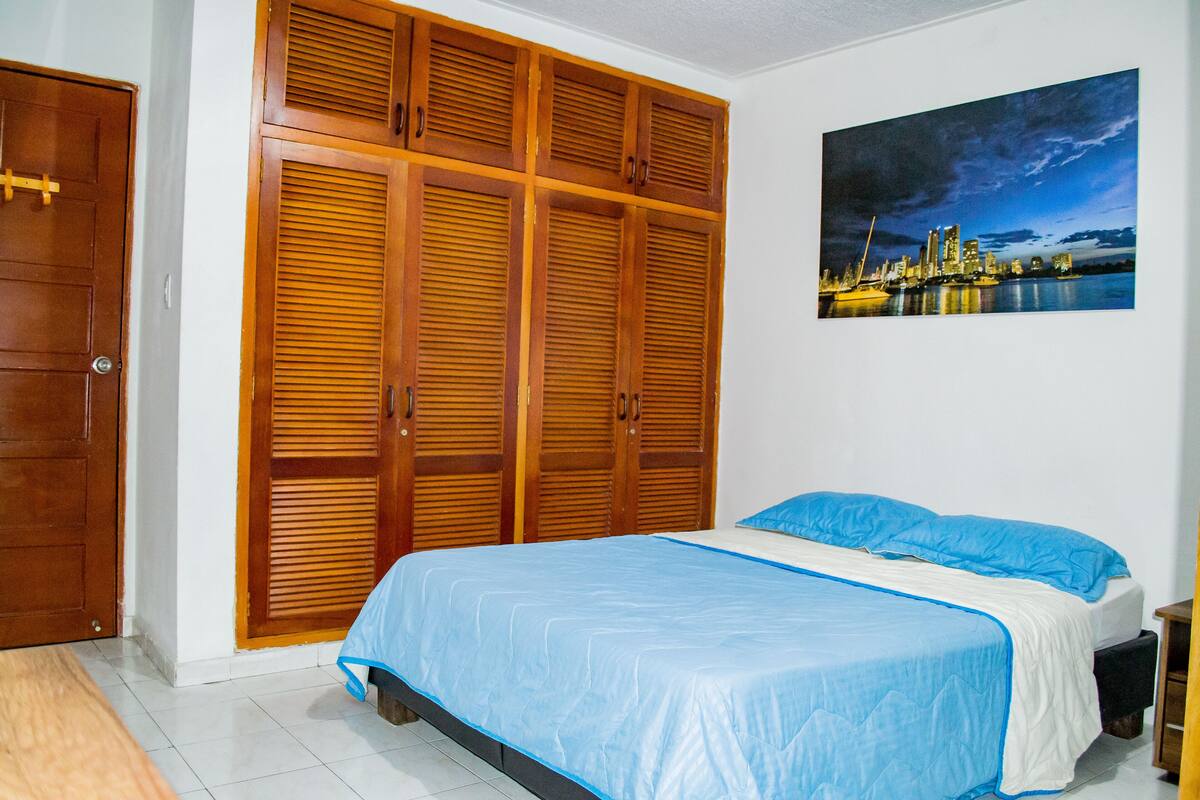 A bedroom with a bed, wooden wardrobe, and a cityscape painting.