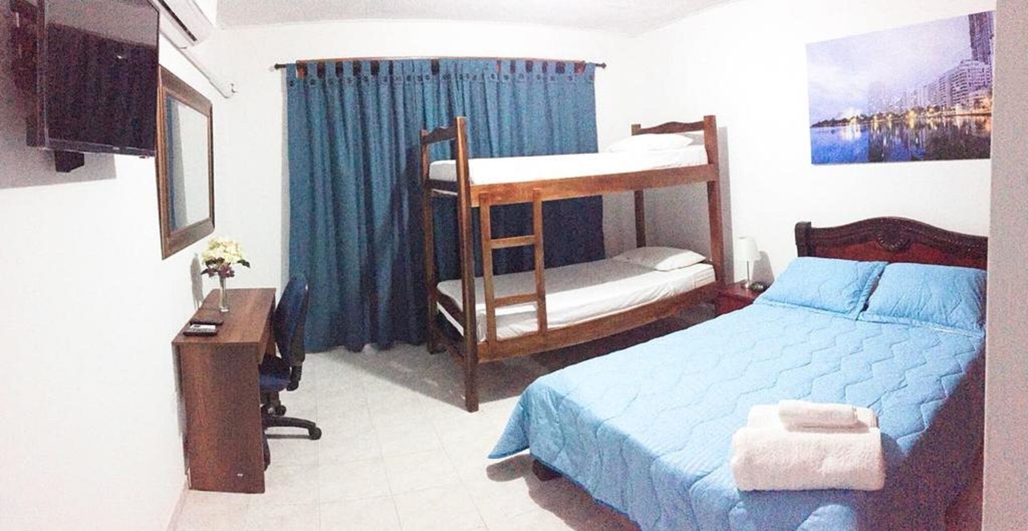 A room with bunk beds, a desk, a chair, a lamp, and a painting on the wall.