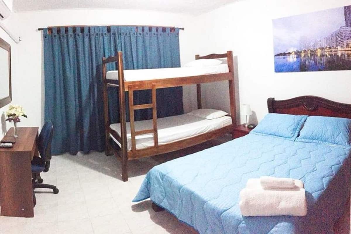 A room with bunk beds, a desk, a chair, a lamp, and a painting on the wall.