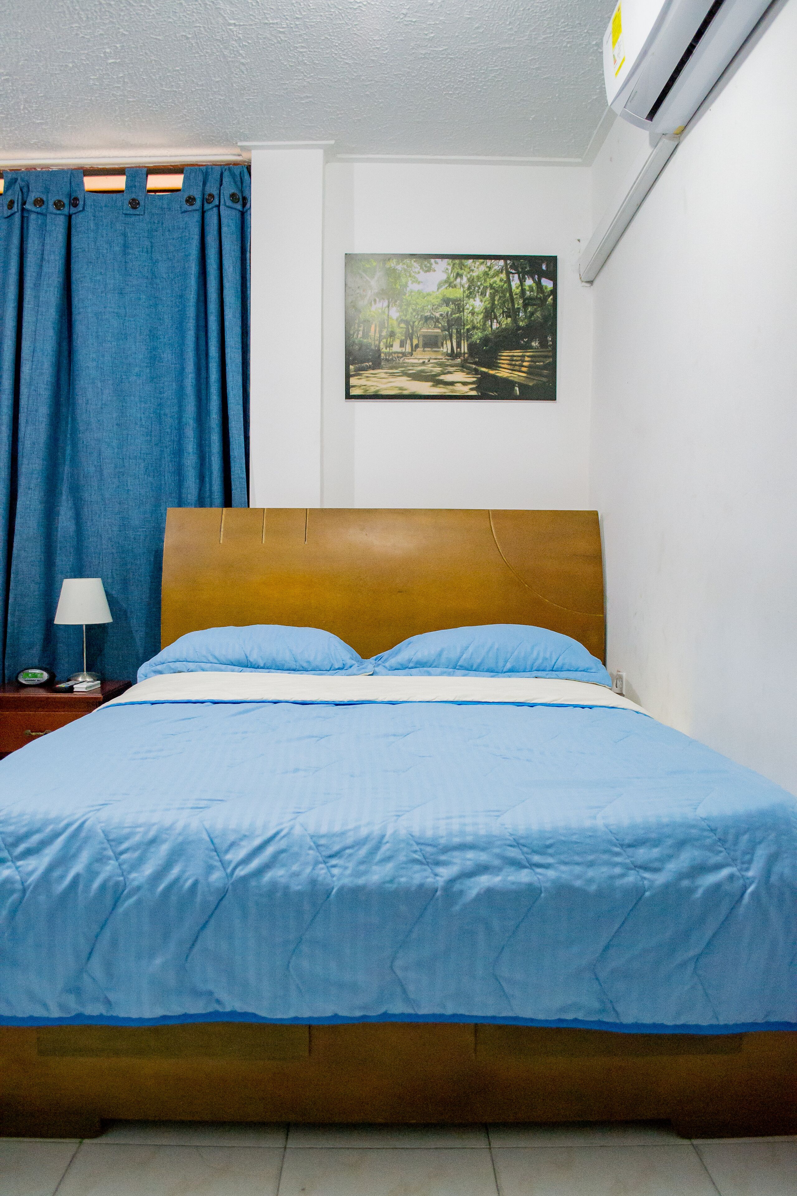 A bed with a wooden headboard, a blue bedspread, and a white pillow.