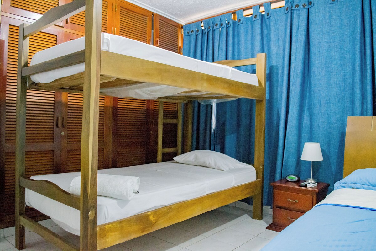 A bunk bed room with a wooden frame, a nightstand with a lamp, and blue curtains.