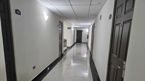 A long, narrow hallway with a tiled floor, doors on both sides, and a fire extinguisher mounted on the wall. - Hotel Plaza del Arco (Monterrey)