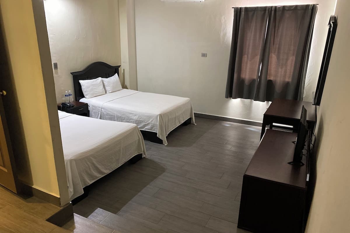 Una habitación de hotel con dos camas individuales, un escritorio con una computadora y un televisor.