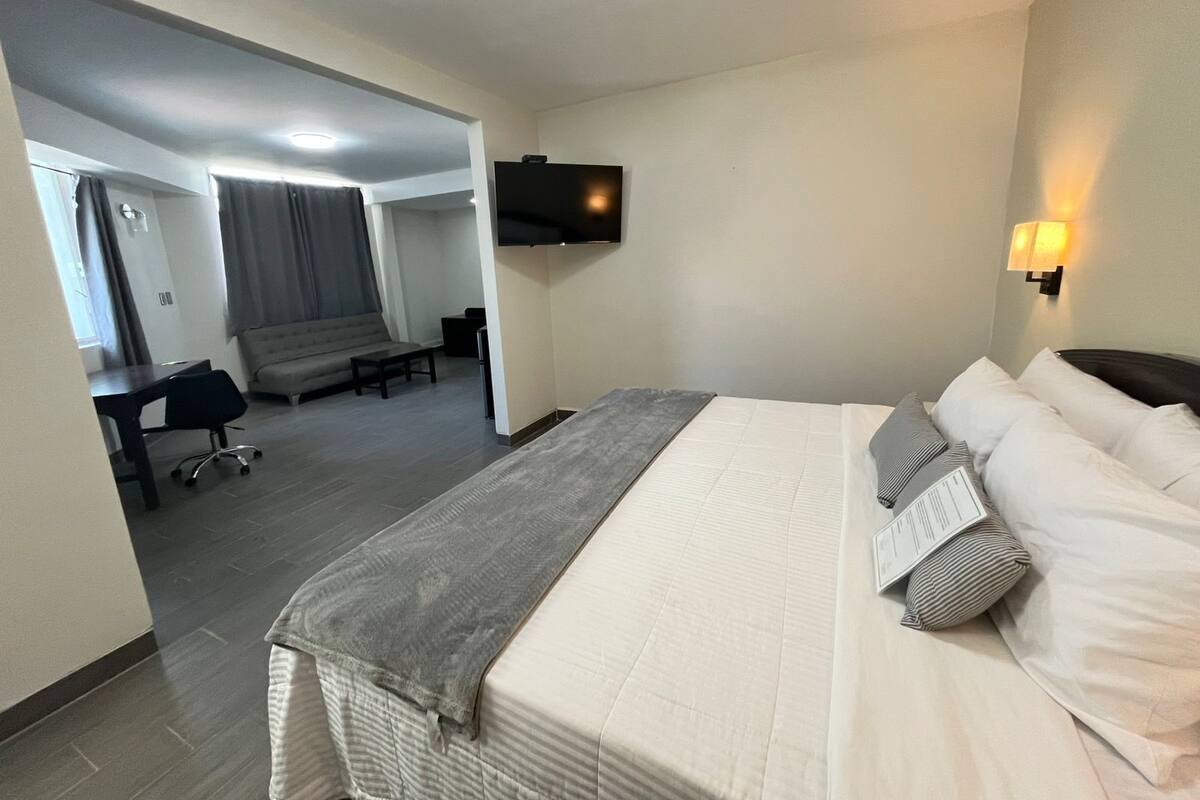 Habitación de hotel con cama, escritorio, silla, televisor y lámpara de pared.