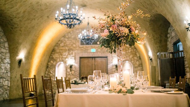 A banquet hall with stone arches, chandeliers, and a table set for a formal event.
