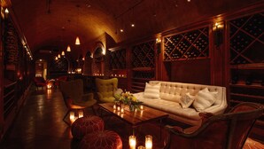 A dimly lit lounge area with a wooden ceiling, a white sofa, leather armchairs, and a coffee table with candles.