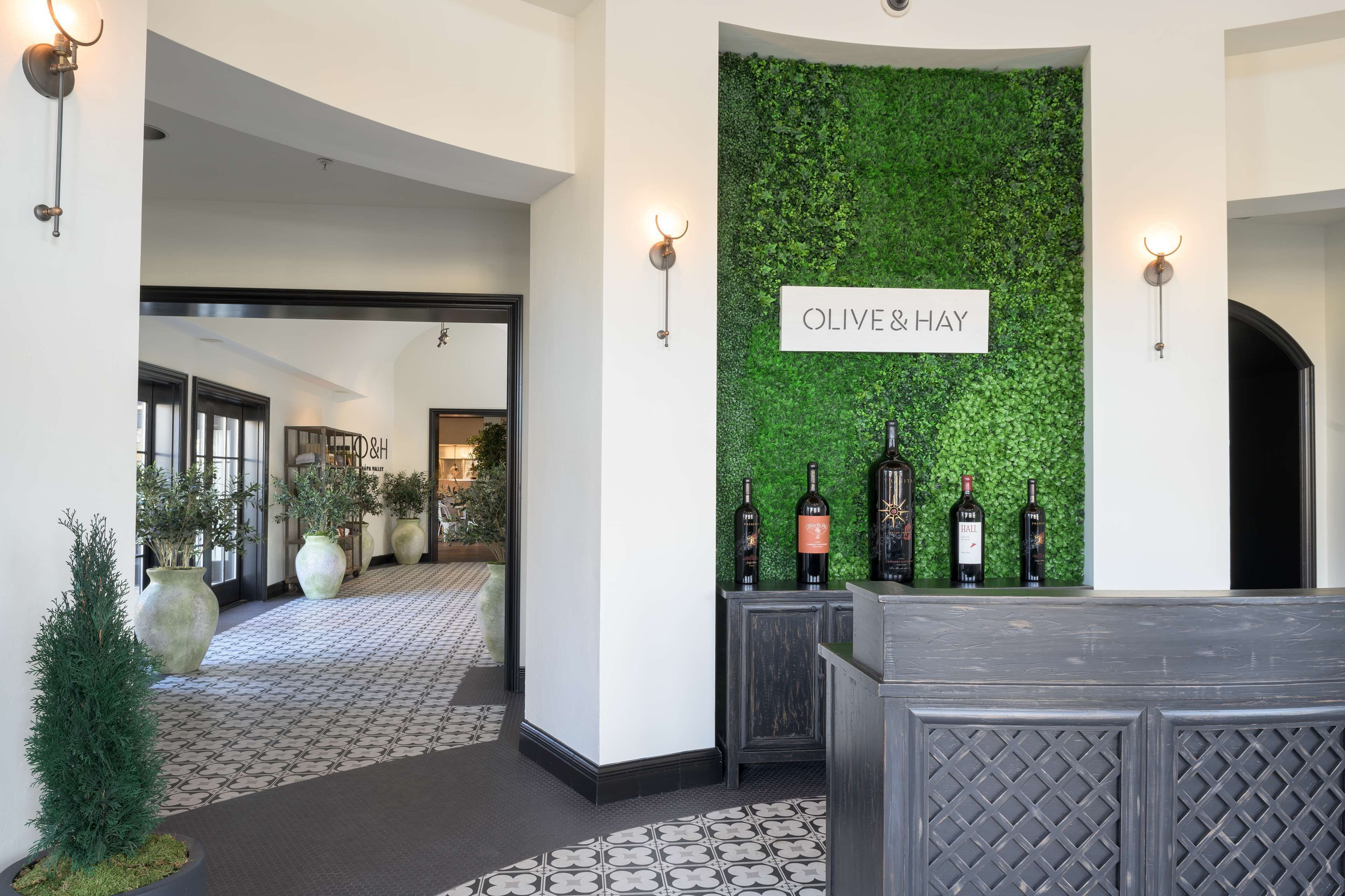 A reception area with a green wall and a sign reading "OLIVE & HAY". There are several wine bottles displayed on a counter.