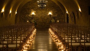 An aisle with rows of chairs and candles, leading to a stone wall with a chandelier.