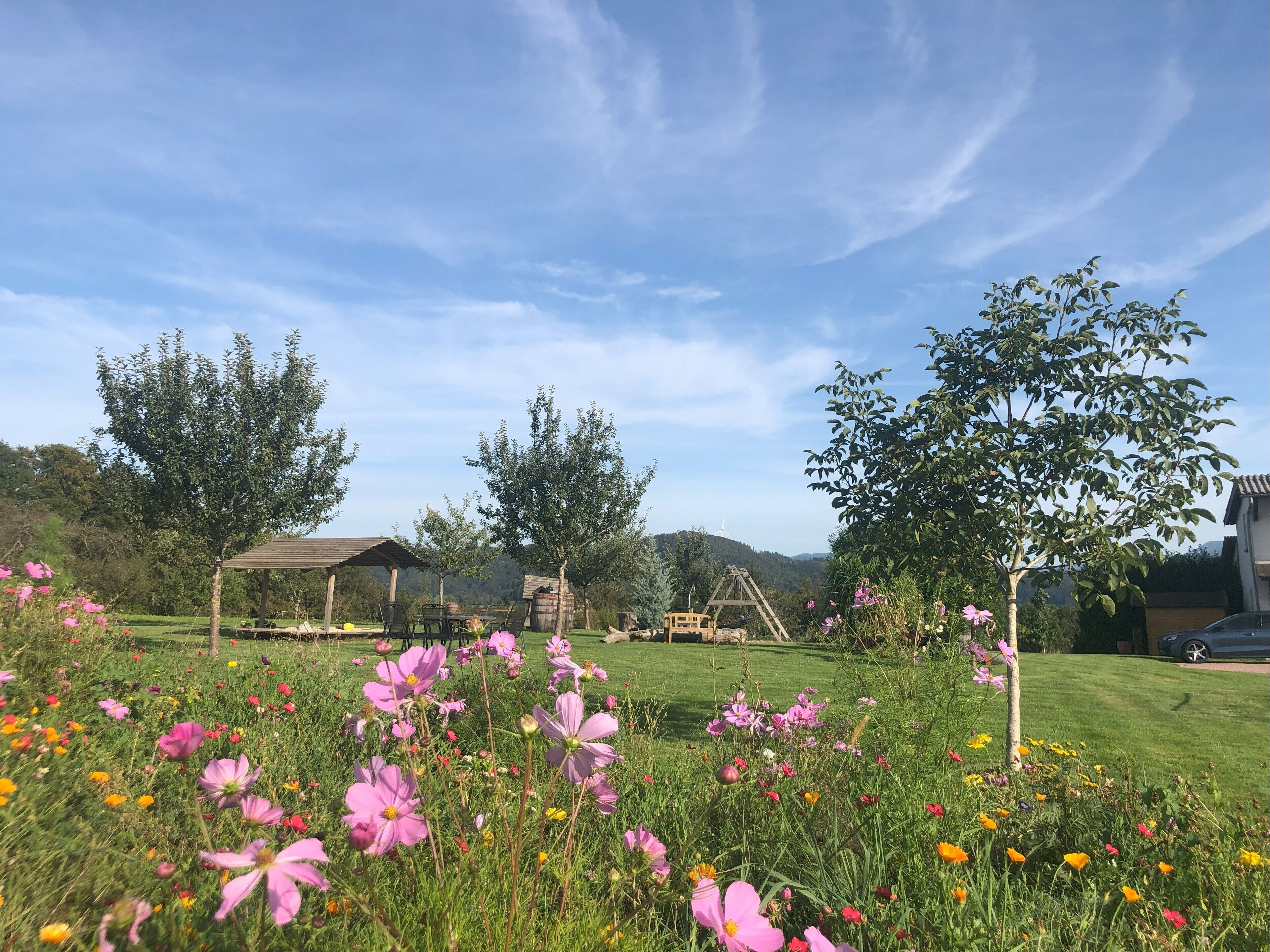 Ein Garten mit einem Pavillon, Bäumen und einer blumenbewachsenen Rasenfläche.
