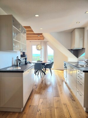 A modern kitchen with a central island, wooden flooring, and a view to the outside.