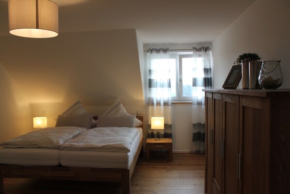 Un dormitorio con cama, lámparas de noche, mesita de noche, armario y ventana con cortinas.
