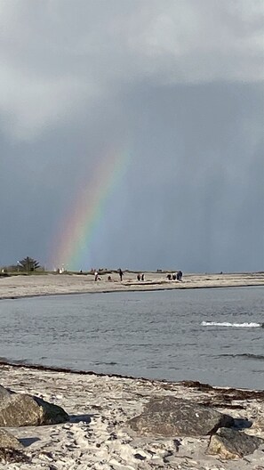 Une plage avec un arc-en-ciel dans le ciel et des gens qui se promènent le long du rivage.