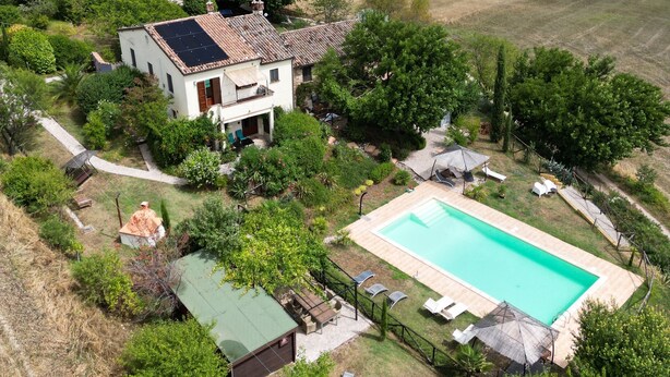 Une maison avec une piscine, entourée de verdure et de collines.