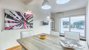 Un comedor moderno con una mesa de madera, un cuadro abstracto y colorido, y un amplio ventanal con vistas al exterior.