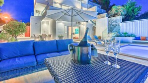 Un área de estar moderna al aire libre con piscina, una botella de champán y dos copas.