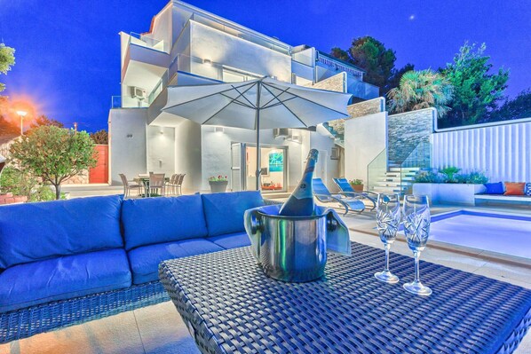 A modern outdoor seating area with a pool, a bottle of champagne, and two glasses.