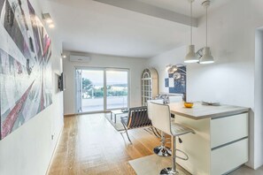 A modern kitchen with a large island, a dining area with a table and chairs, and a view through the glass door.
