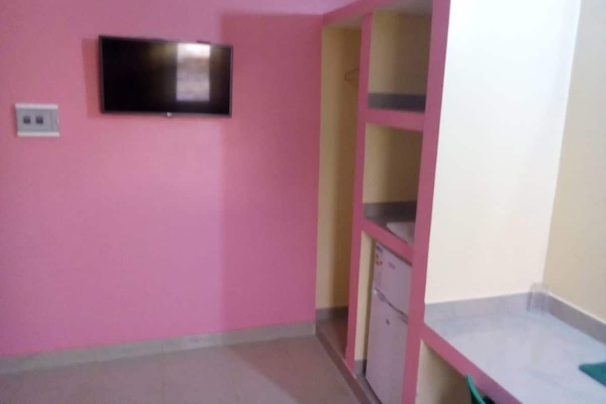 A room with pink walls, a flat-screen TV mounted on the wall, and a built-in cabinet with a refrigerator.