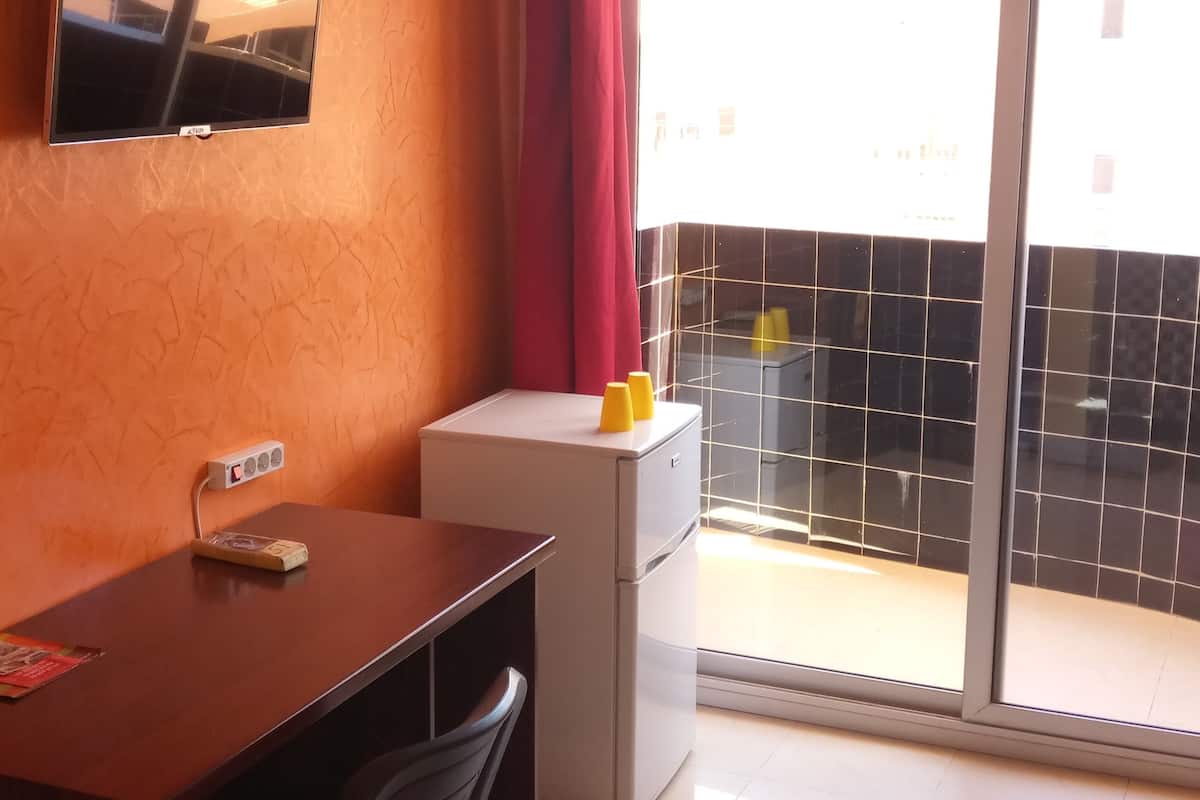 A room with a desk, chair, and a small table with two yellow cups. There is a window with a view of a building outside.