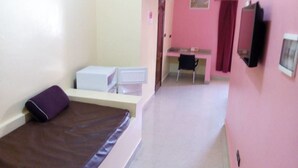 Quarto com cama, escrivaninha e cadeira. Há uma televisão fixada na parede.