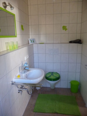 Un baño con lavamanos, inodoro, alfombra verde y un cubo de basura verde.