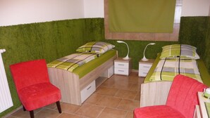 A bedroom with two beds, a red chair, and a green wall.