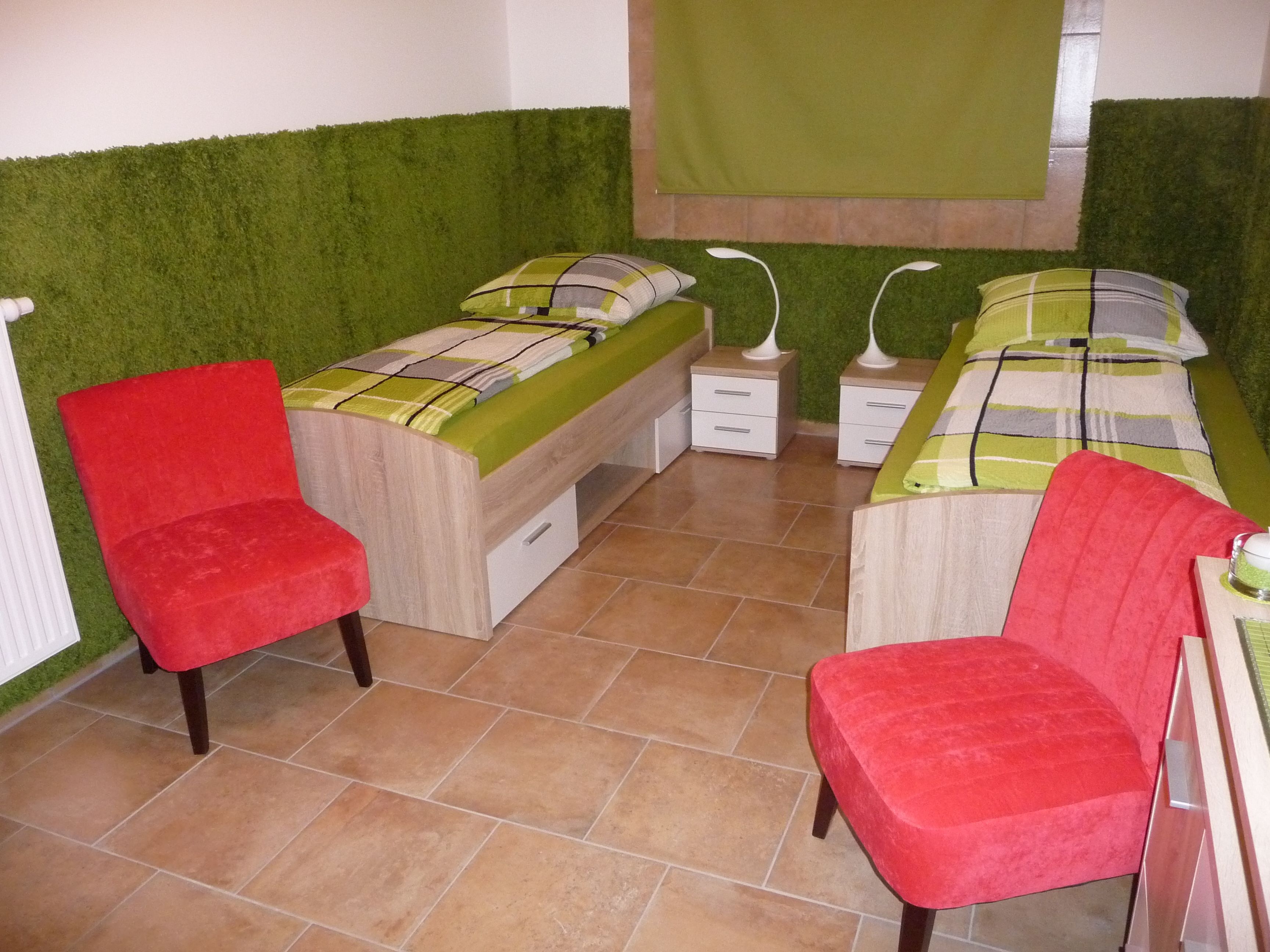 Een slaapkamer met twee bedden, een rode stoel en een groene muur.