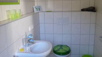 Een badkamer met een wastafel, toilet, groene mat en een groene prullenbak.