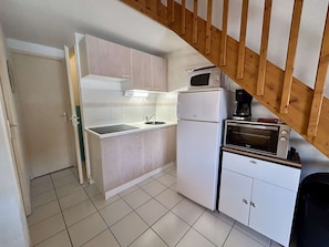 Een compacte keuken met een ingebouwde magnetron, een kleine oven en een spoelbak.