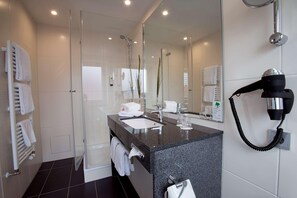 Un baño moderno con cabina de ducha de vidrio, un lavabo con espejo y un secador de pelo fijado a la pared.