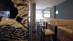 Un restaurante con una decoración moderna, que destaca una pared texturizada única, una zona de estar con mesas y sillas, y un espejo grande en la pared.
