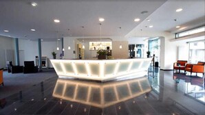 Una moderna recepción con mostrador central, zona de estar y amplios ventanales que dejan entrar luz natural.