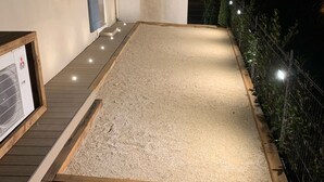 Eine Holzterrasse mit Kiesfläche, umgeben von einer niedrigen Mauer und einem Zaun mit Beleuchtung.