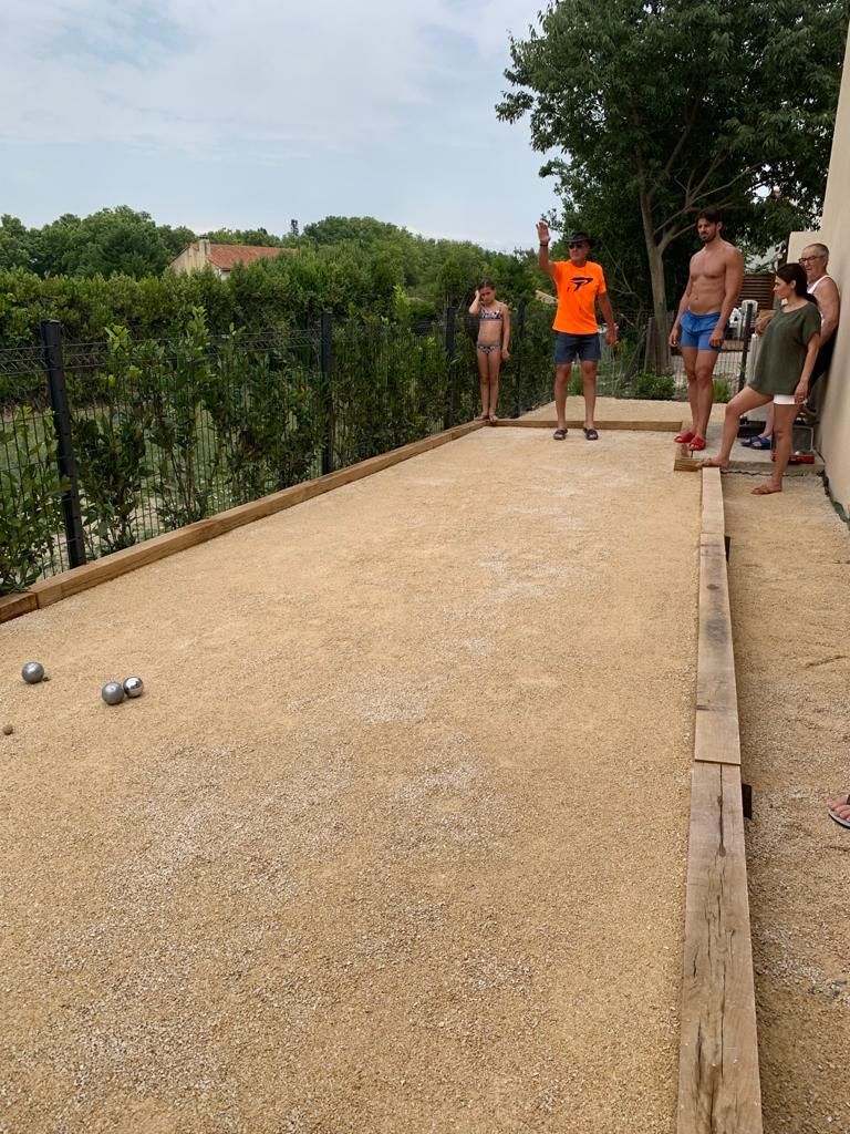 A billiards table with balls and a wooden edge, surrounded by a hedge and a building.