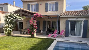 Ein Haus mit Swimmingpool, einer Terrasse mit Stühlen und einem Garten mit Blumen.