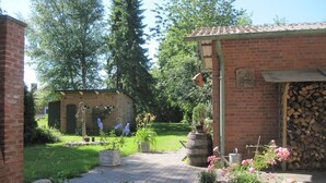 Un edificio in mattoni con un'area giardino, comprensivo di un muro in pietra, piante in vaso e una botte di legno.