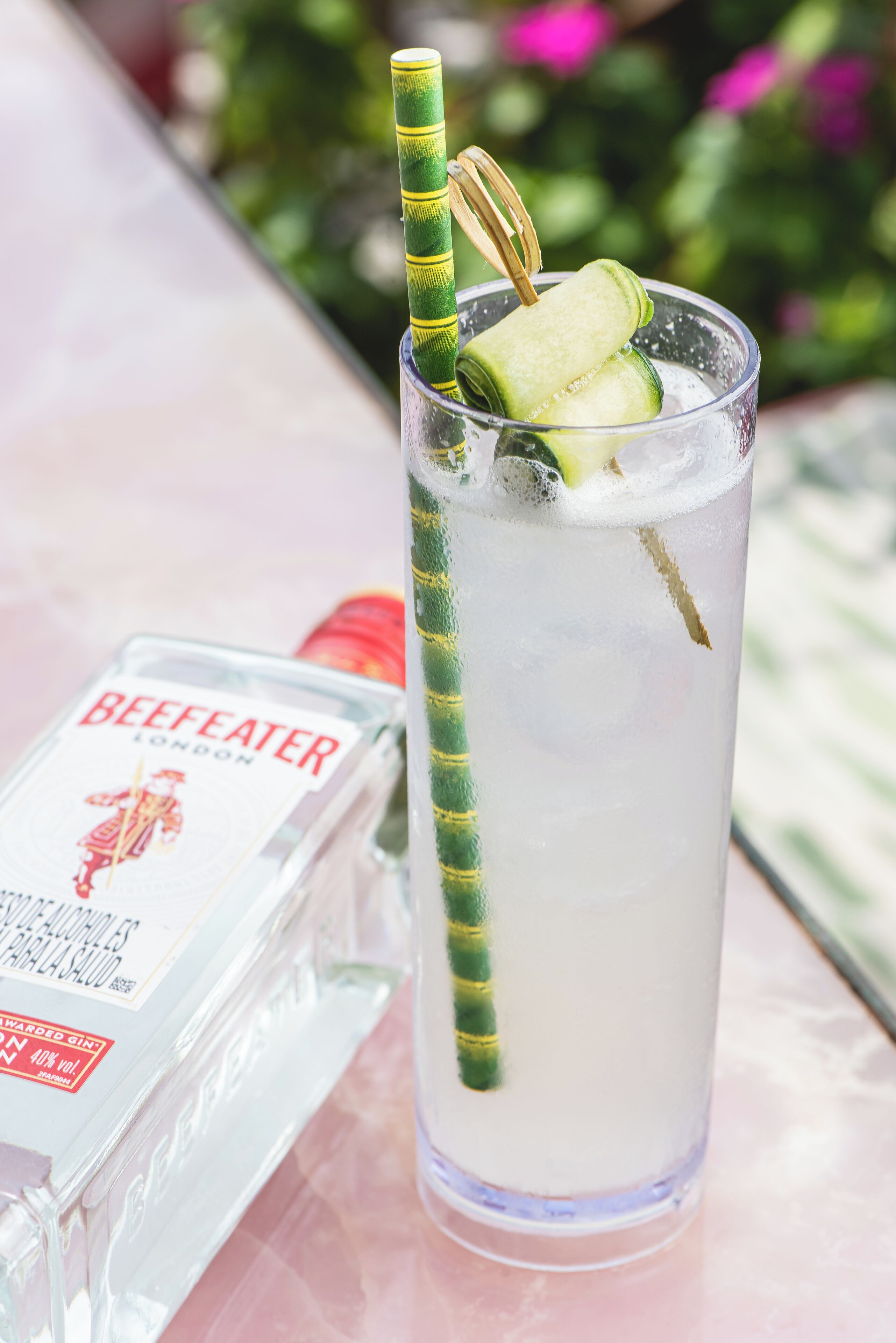 A tall glass with a straw and cucumber slices, next to a bottle of BeefEater London gin.