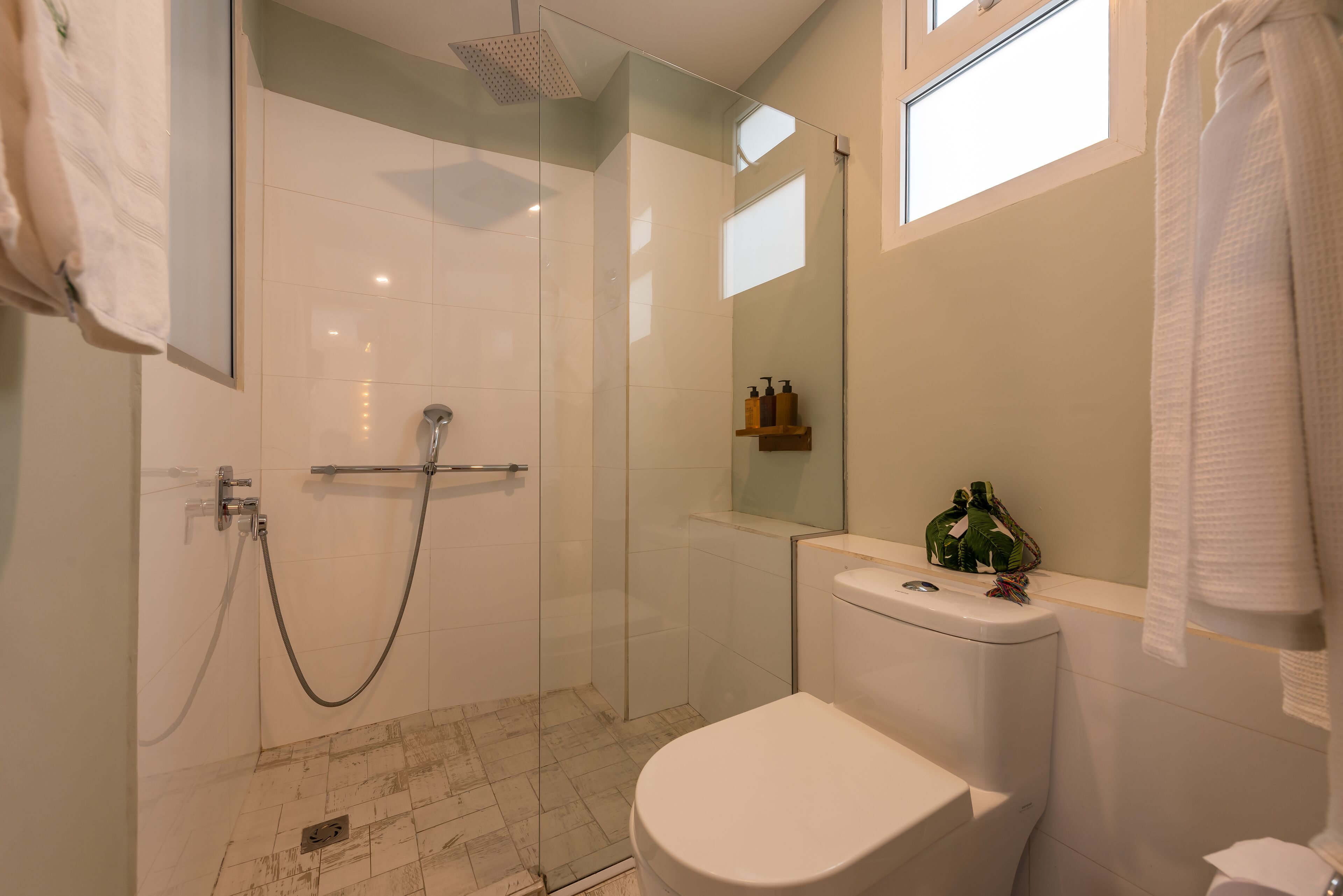 Un baño moderno con ducha de vidrio, inodoro blanco y un pequeño estante con artículos de aseo.