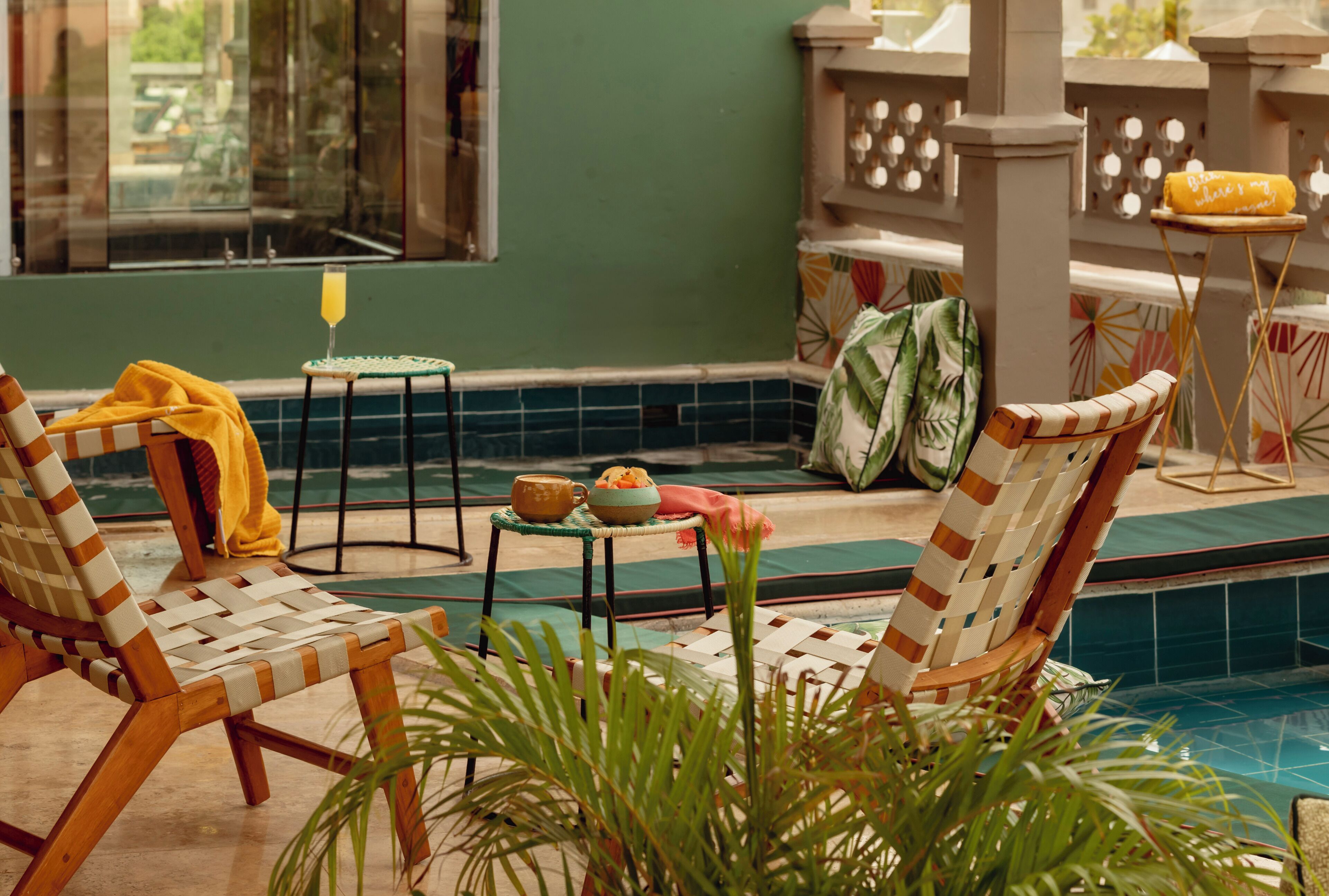 A poolside area with two wicker lounge chairs, a small table with a drink, and a towel on a stand.