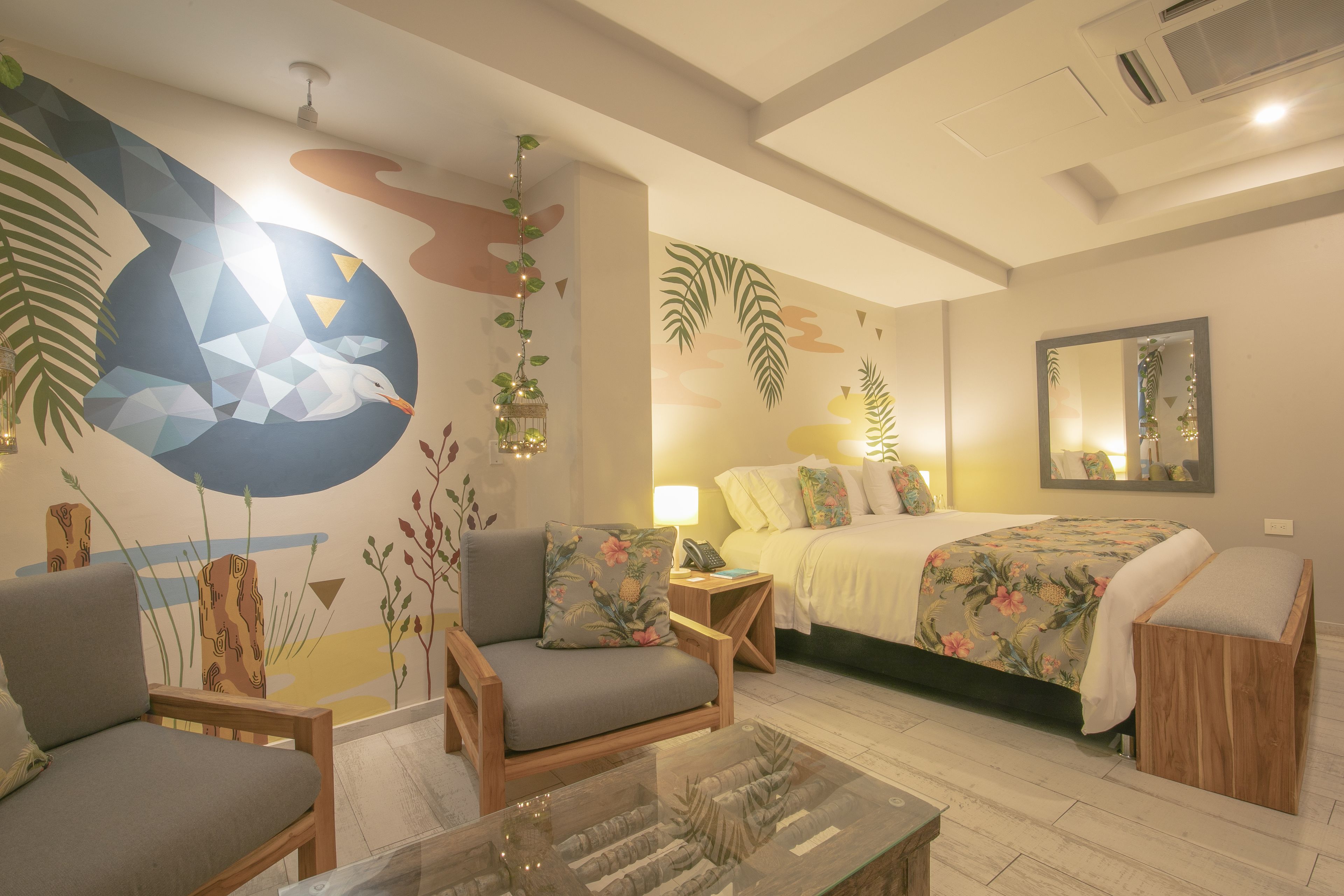Una moderna camera d'hotel con un letto, due poltrone, un tavolino in vetro e un affresco sulla parete.