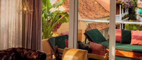 Une pièce avec un canapé en cuir, un fauteuil jaune et une table basse en verre. Une grande fenêtre offre une vue sur les bâtiments et sur un jardin.