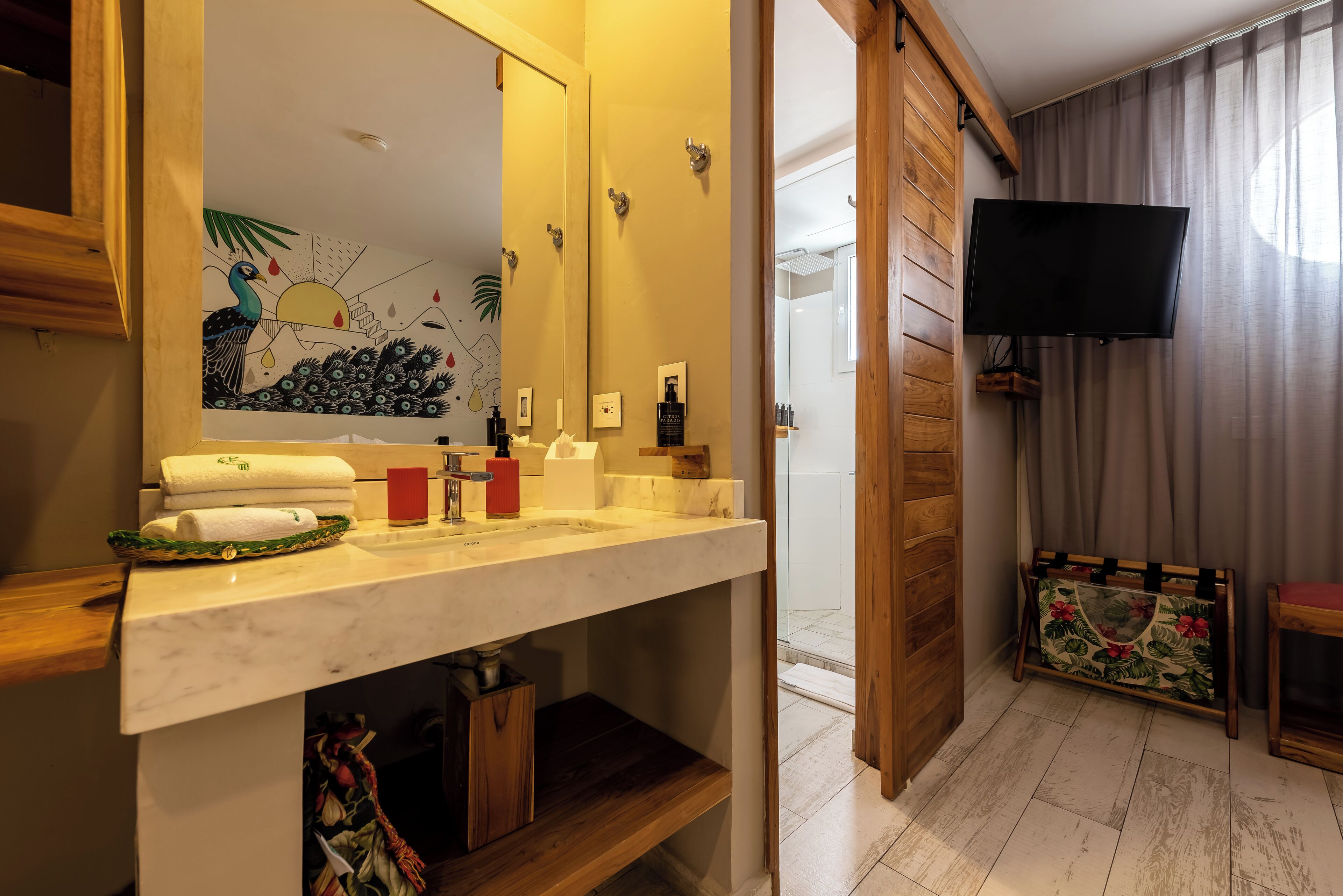 A bathroom with a marble sink, a mirror, a towel rack, a shower area, and a television mounted on the wall.