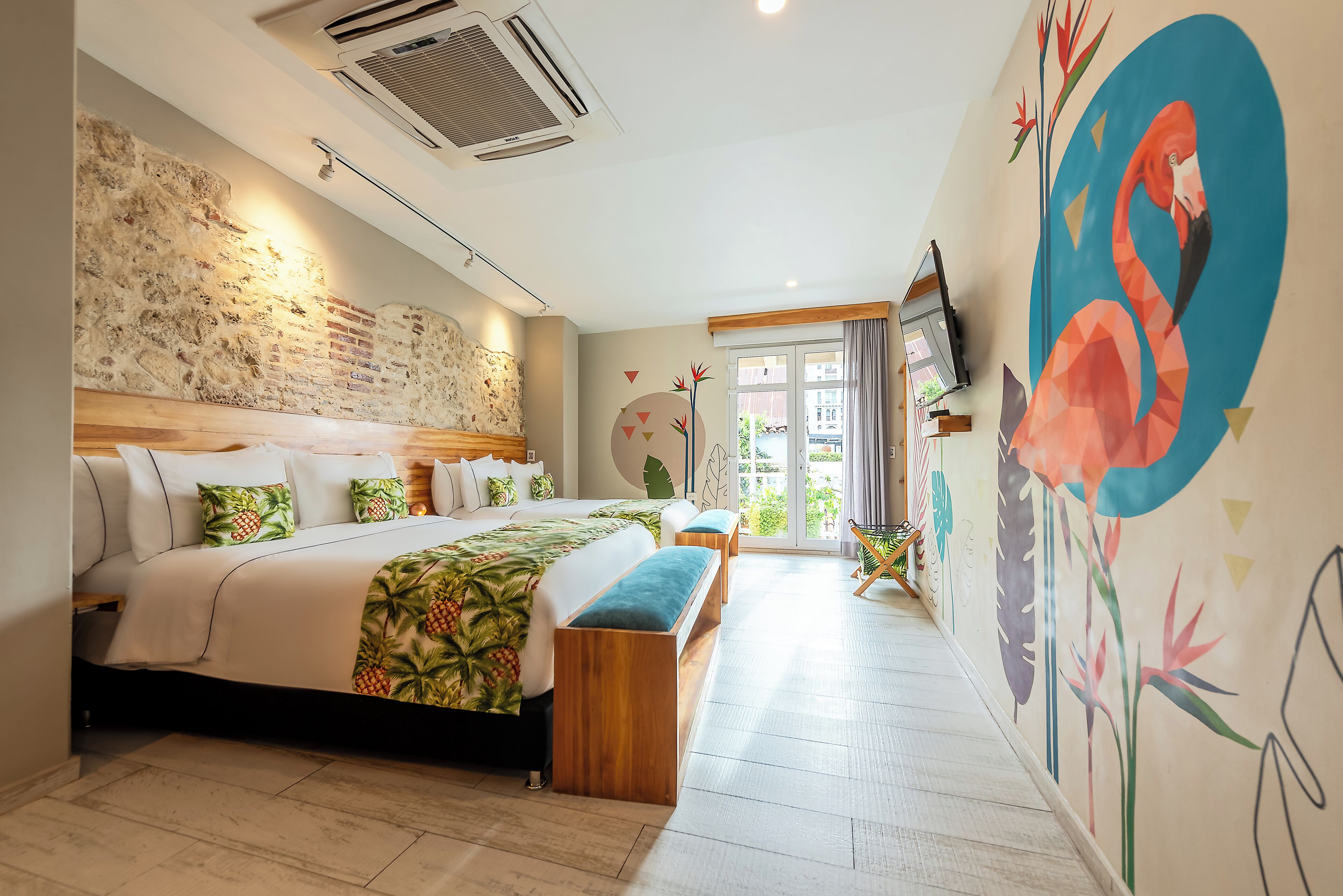 A modern hotel room with a large bed, a wooden bench, a stone wall, and a mural of a flamingo.