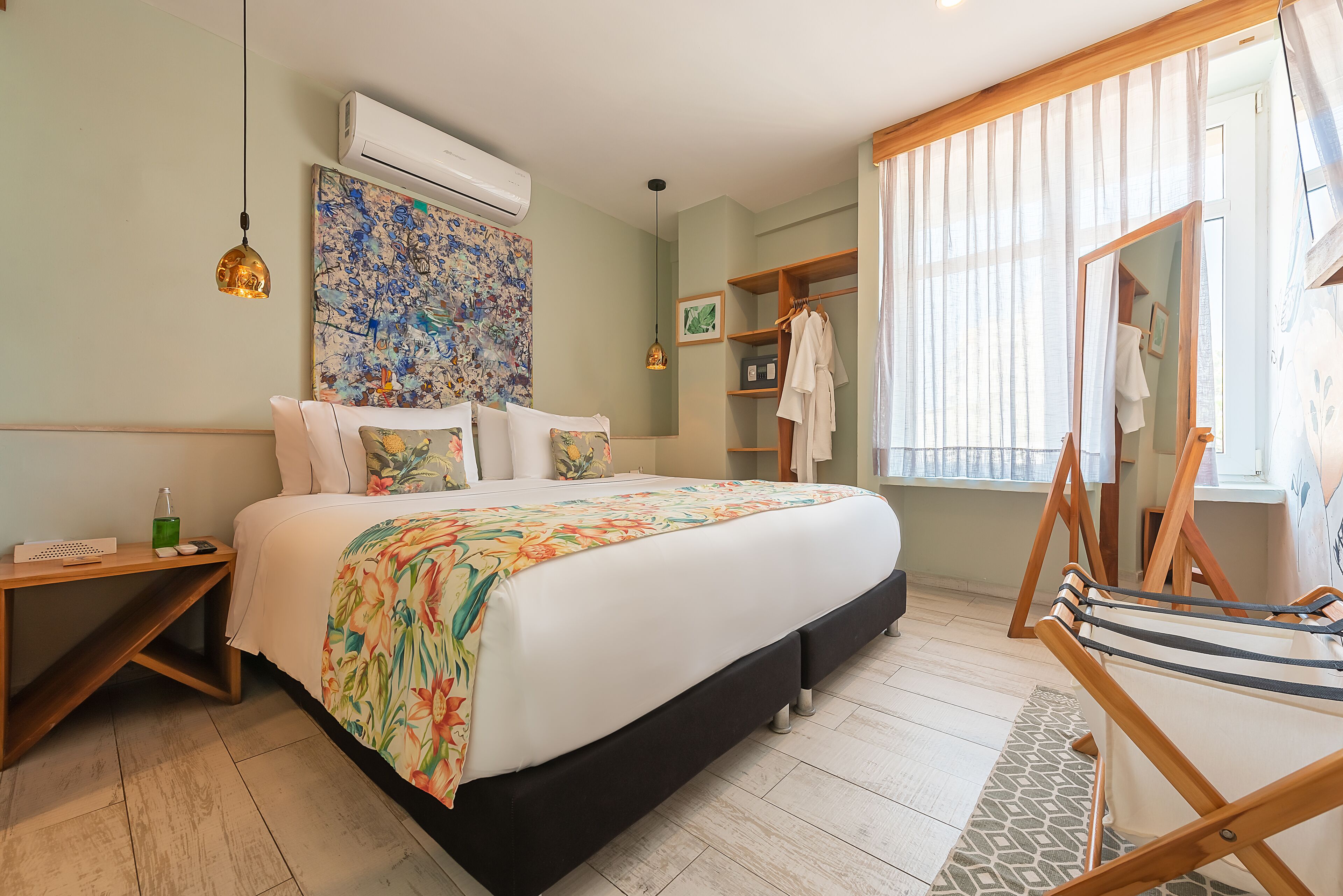 A bedroom with a bed, a wooden nightstand, a hanging light, a painting, a wardrobe, and a mirror.