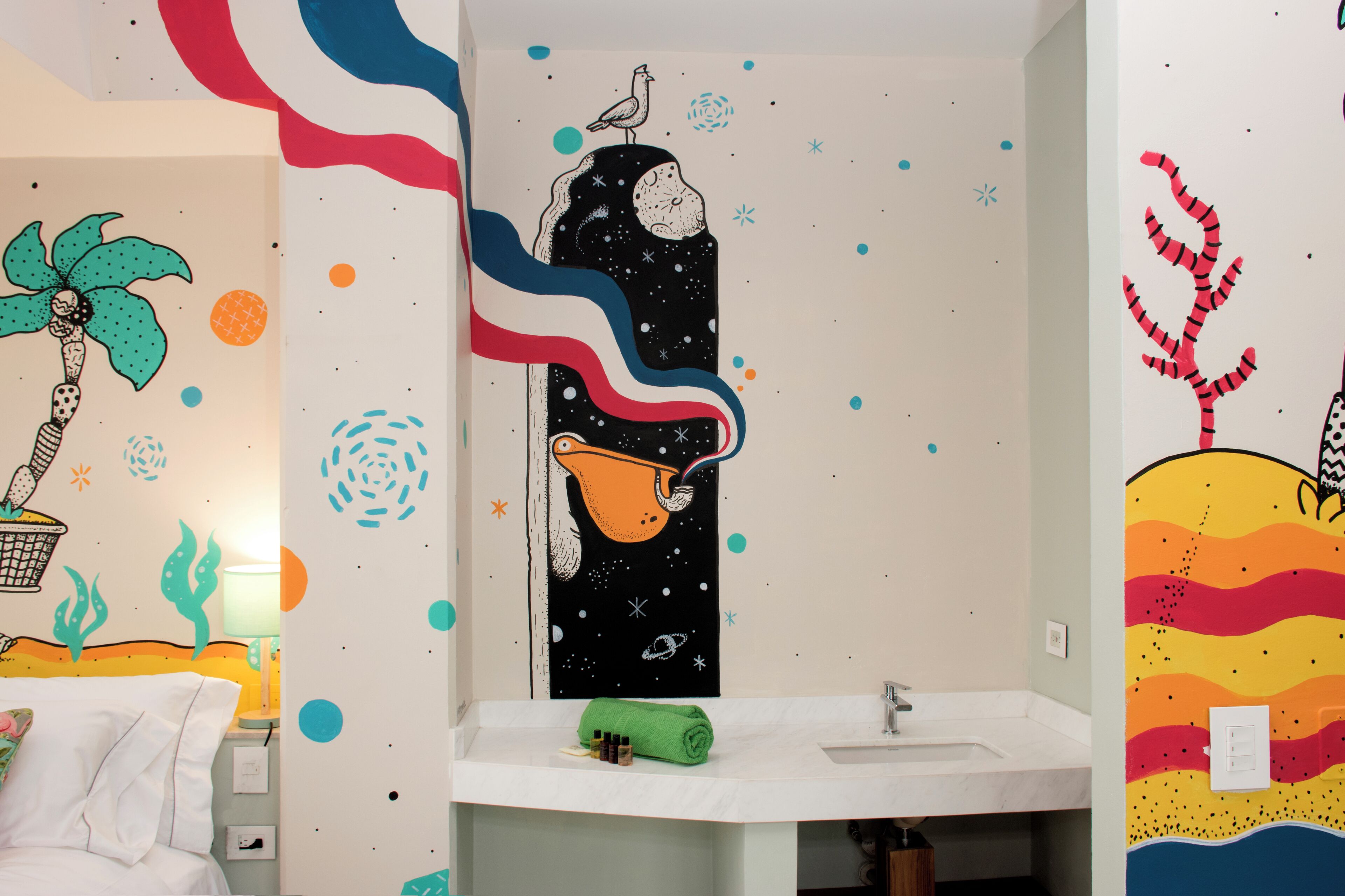 A bathroom with a white sink, a green towel, and a wall with colorful, abstract art.
