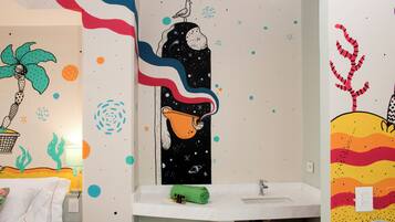A bathroom with a white sink, a green towel, and a wall with colorful, abstract art.