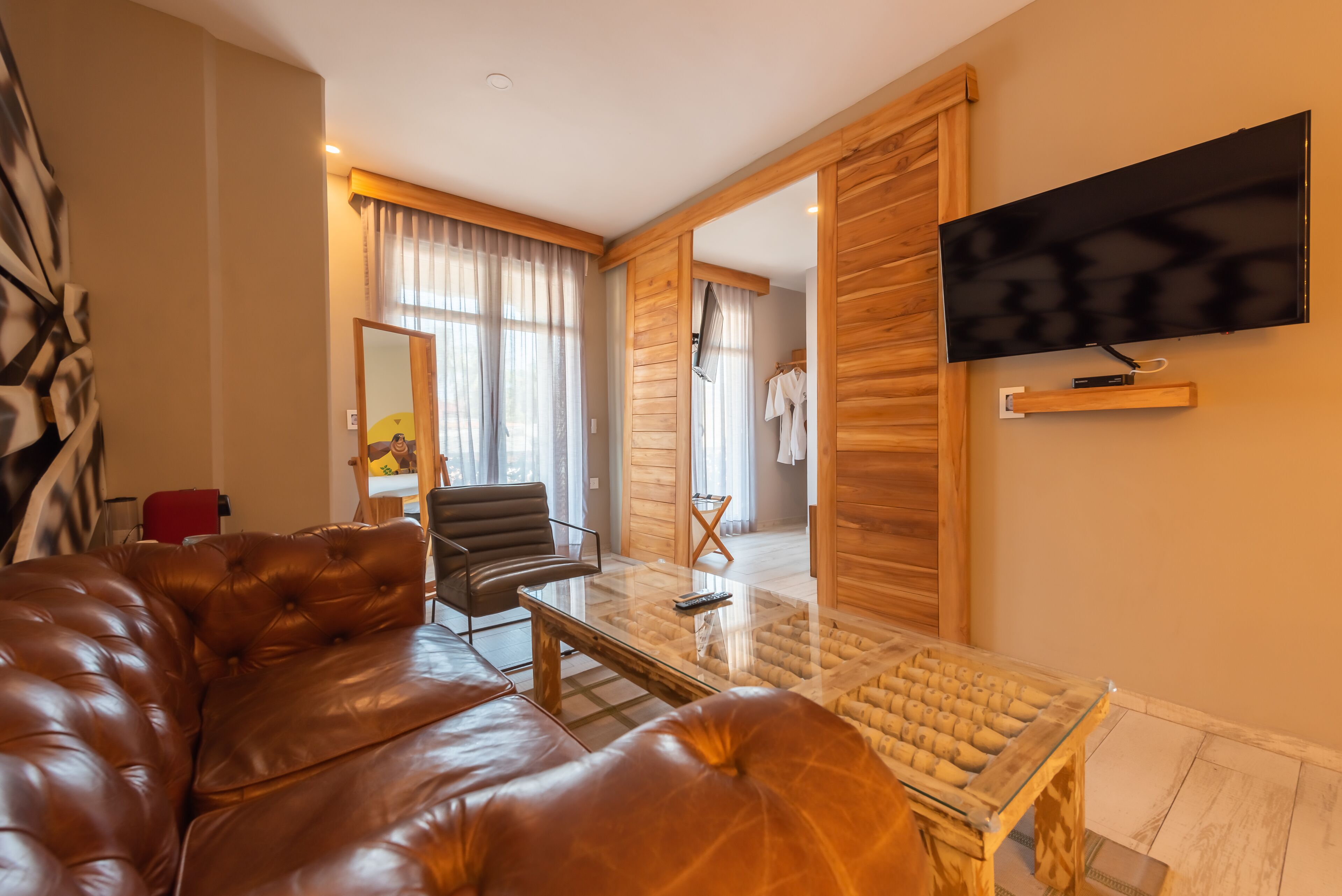 A modern living room with a leather sofa, a glass coffee table, and a flat-screen TV mounted on the wall.